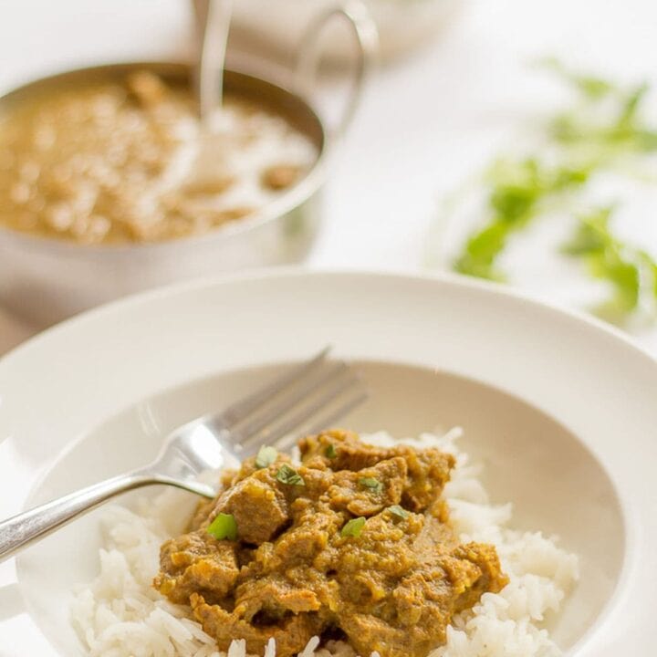 Mild beef curry served on a bed of rice. Balti dishes of beef curry and rice in the background.