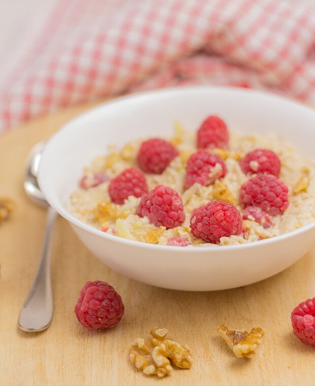 A bowl of raspberry bircher overnight oats decorated with raspberries and chopped walnuts.