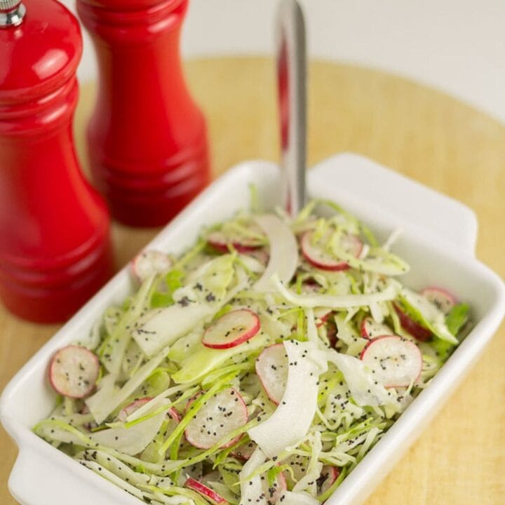 Cabbage and radish slaw served in a white rectangular dish with a spoon in. Salt and pepper cellars beside.