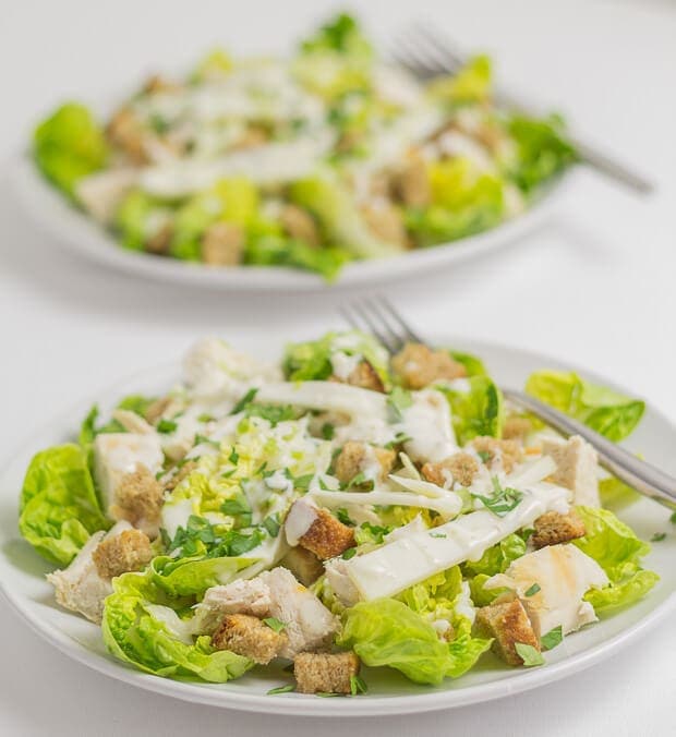 Close up of a plate of chicken Caesar salad with a fork on and another plate in the background.