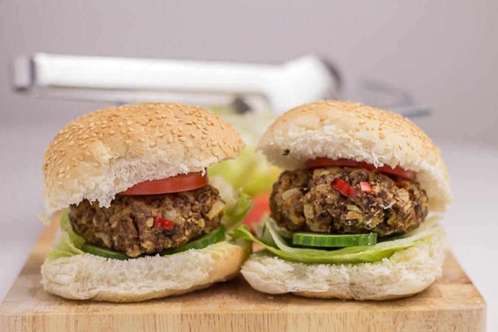 Two home-made quorn burgers in burger buns with lettuce and tomato garnish side by side on a chopping board.