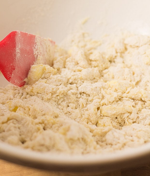 Spatulata stirring flour, butter and egg mixture of English muffins in a large mixing bowl.
