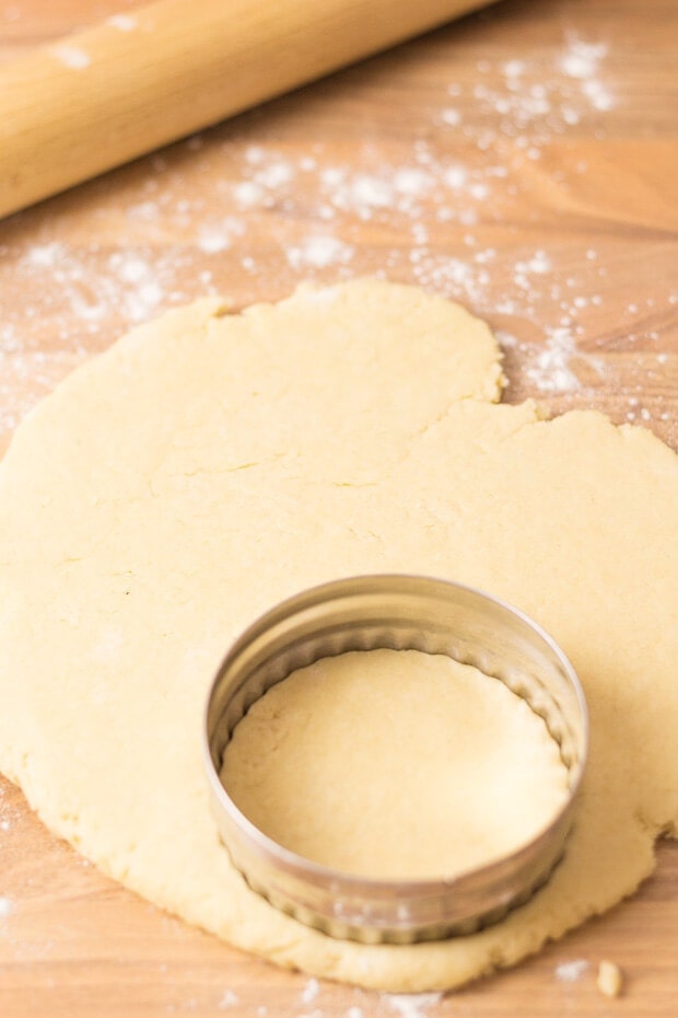 Ball of dough rolled out and being cut into muffin shapes using a round pastry cutter.