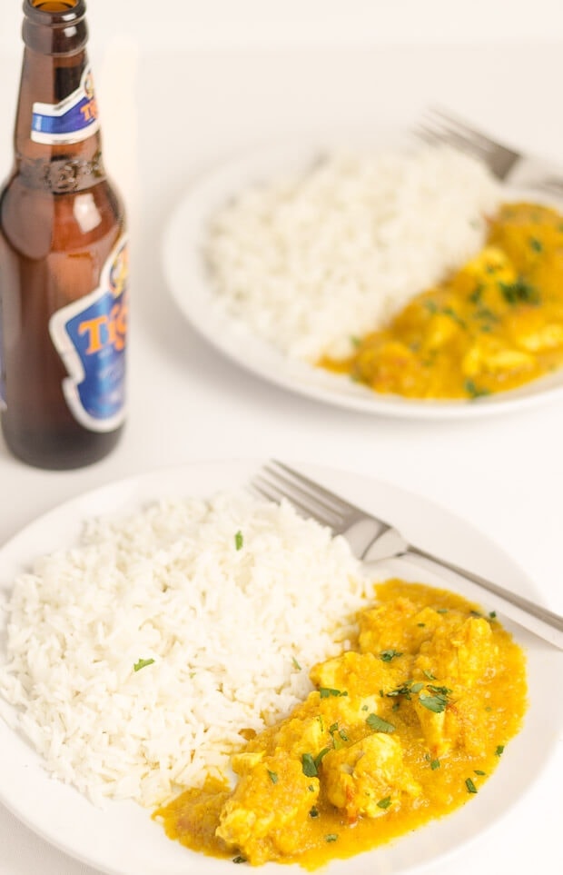 CLose up of two plates of chicken curry in a hurry served with rice and a bottle of beer in between.