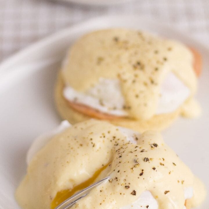 A square plate with two healthy eggs benedict servings. One with a fork breaking open the egg to show the runny yolk.