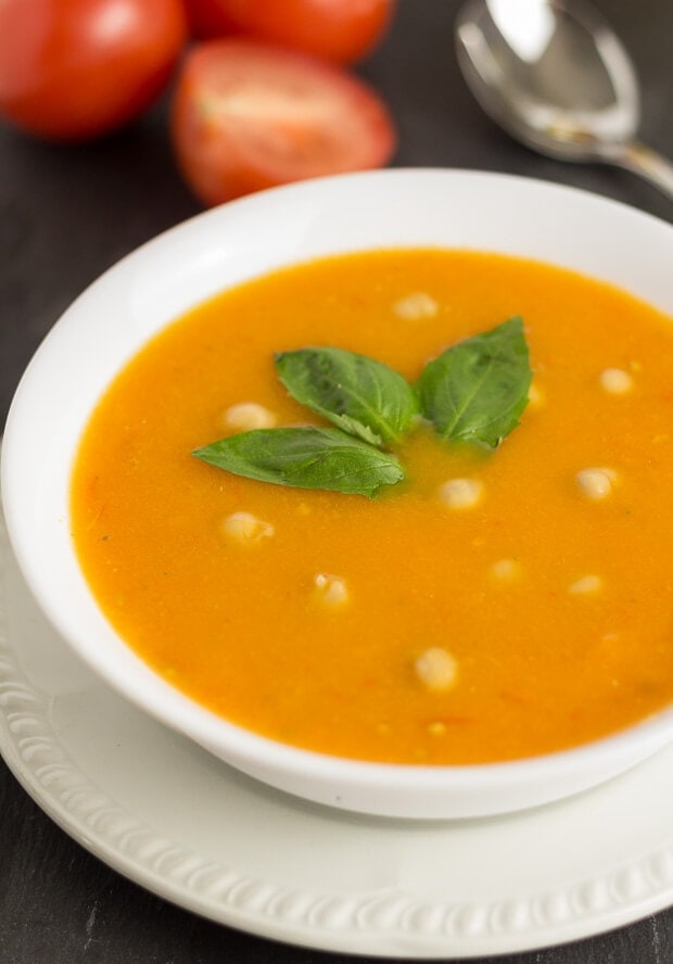 Close up of a bowl of tomato and chickpea soup garnished with a sprig of basil.