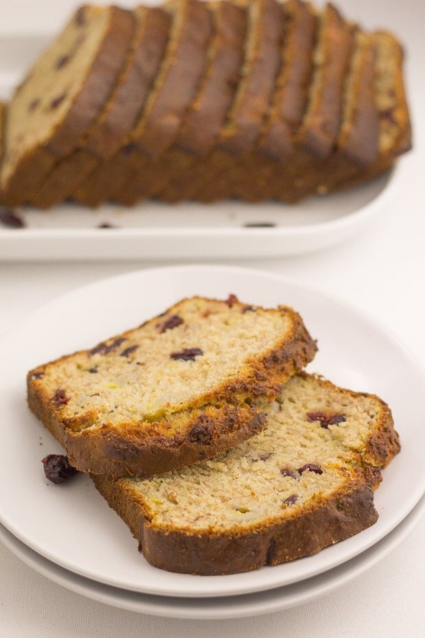 Close up of a plate of two slices of cranberry banana bread. The rest of the sliced loaf on a plate in the background.