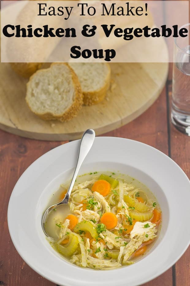 A bowl of simple chicken and vegetable soup in front of a board of sliced bread on it.