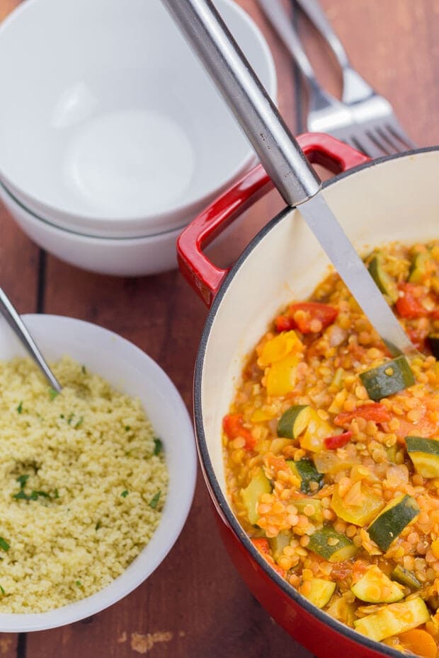 Birds eye view of side by side Mediterranean vegetable casserole and a bowl of couscous with spoons in. Empty serving bowls and forks at the top.