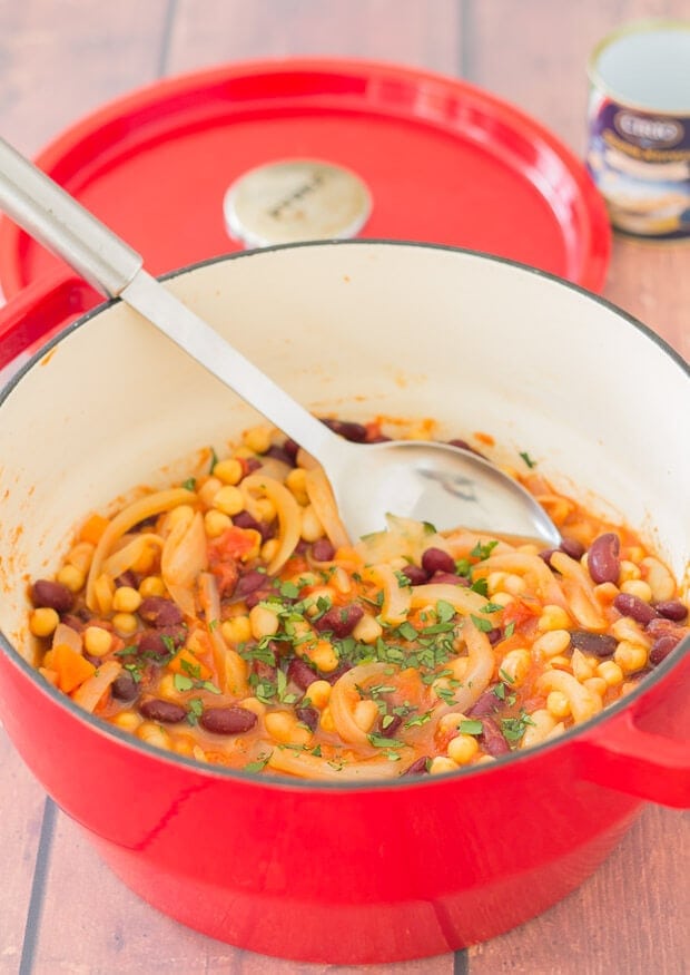 Close up of bean and tomato stew served in a casserole pot with a serving spoon in.