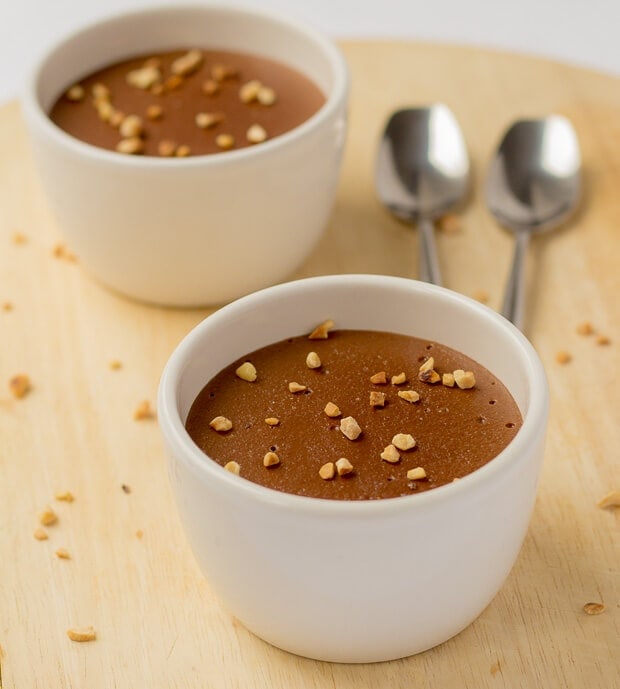 Close up of two ramekins of semolina chocolate pudding. Two teaspoons in the right background.