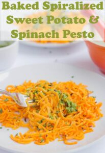 A plate of baked spiralized sweet potato with spinach pesto and a fork lifting up some of the sweet potato.