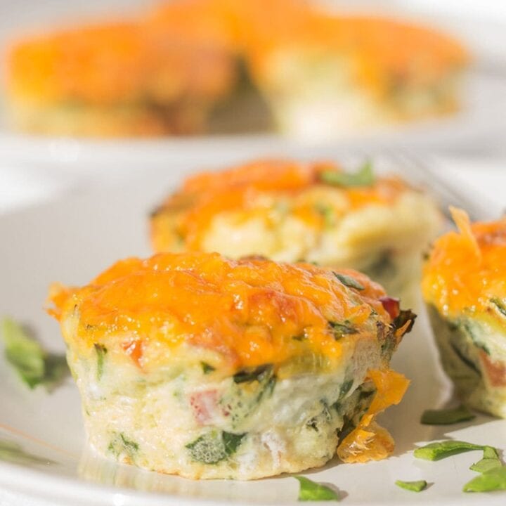 A plate of three Mediterranean breakfast egg muffins. Another plate with three muffins on in the background.