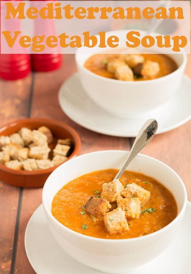 Two bowls of Mediterranean vegetable soup one in front of the other served with croutons. Soup spoons in them and they're ready to eat.