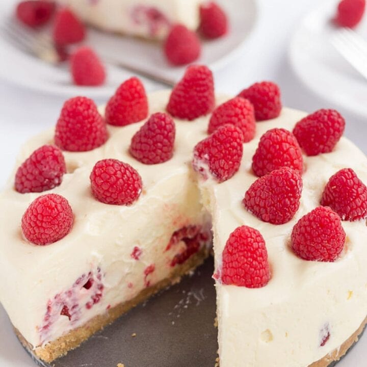 White chocolate and raspberry cheesecake on a plate with a slice taken out of it. Slice on a plate in the background.