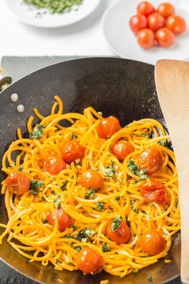 Butternut squash noodles with spring pesto and roasted tomatoes cooked in a wok.