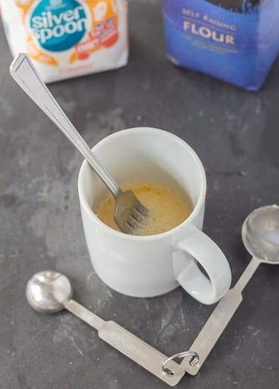 A mug with beaten egg and milk added to the melted butter and a fork in.