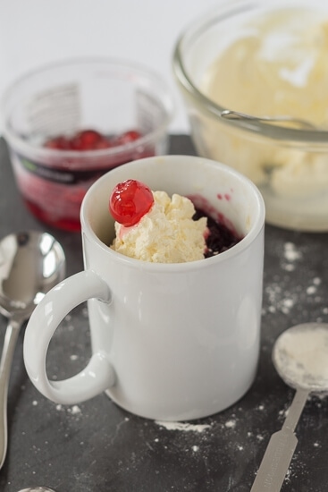 Cherry sponge mug cake decorated with whipped cream and a cherry.