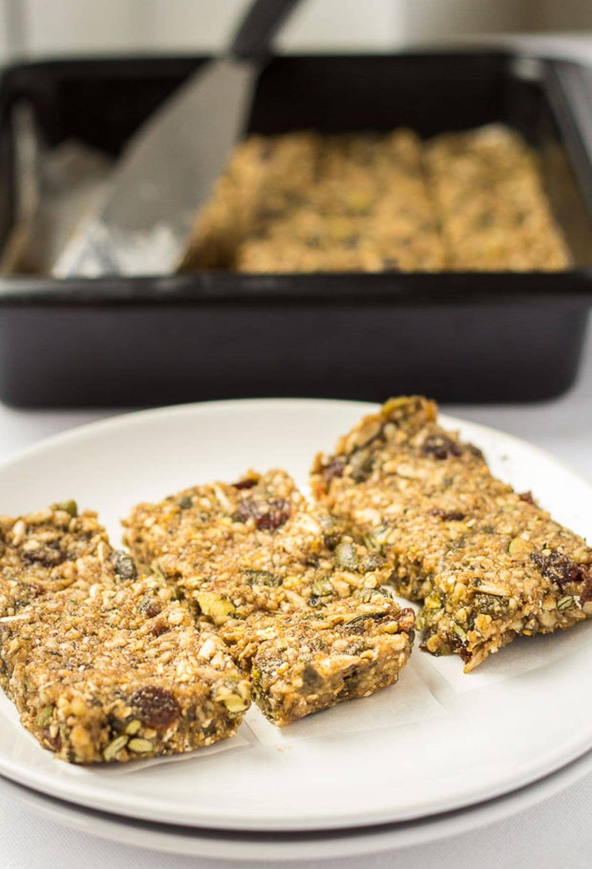 Three no bake banana energy bars on a plate with the rest in a baking dish in the background.