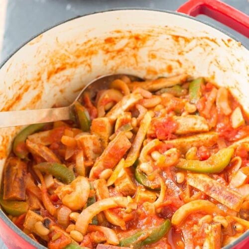 View of cooked chicken sausage casserole in a large casserole pot with a serving spoon in.