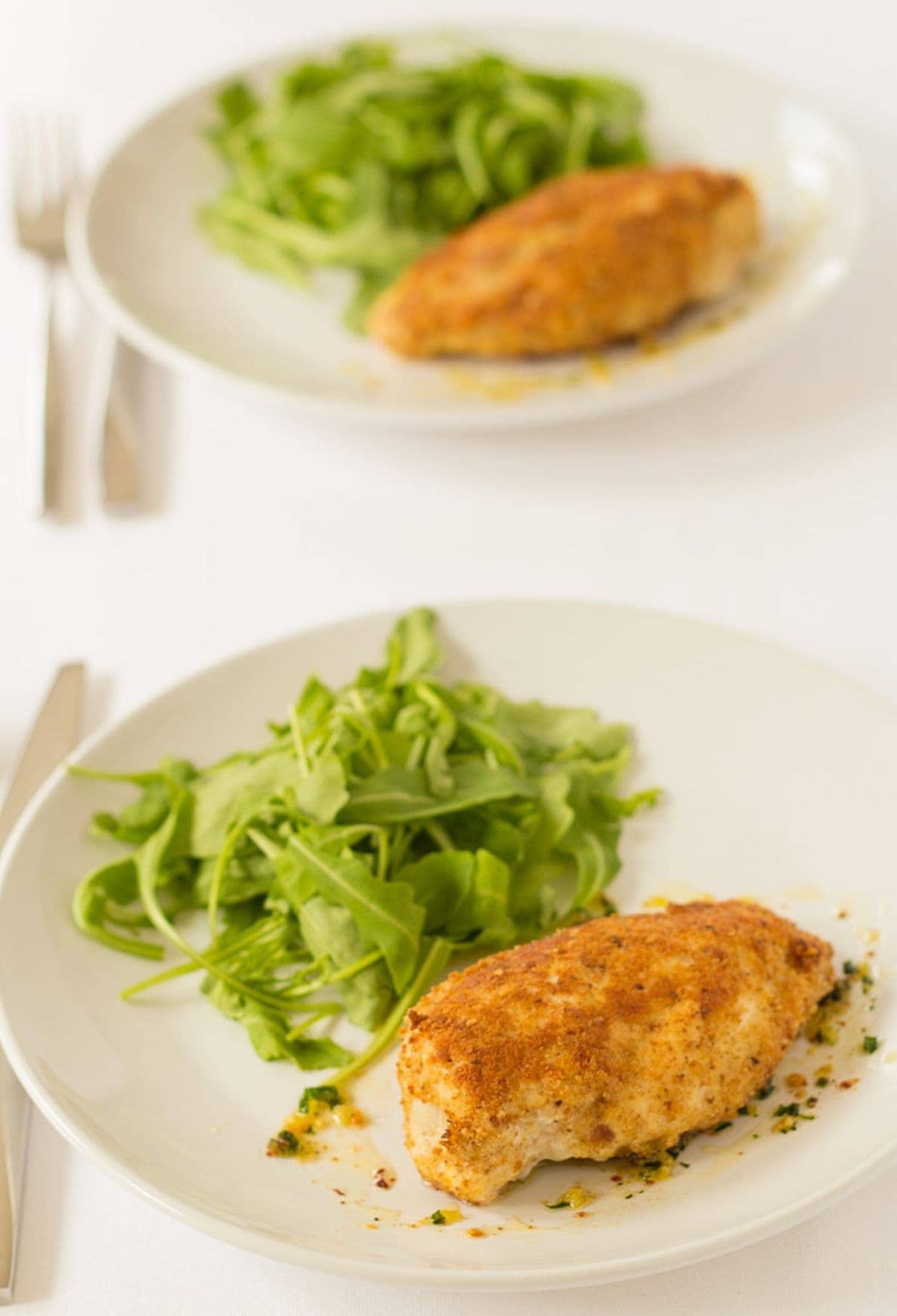 Two plates of baked chicken kievs served with lettuce on one in front of the other with knifes and forks beside.