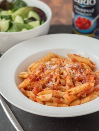 A plate of easy pasta arrabiata. Tin of tomatoes and a green salad in the background.