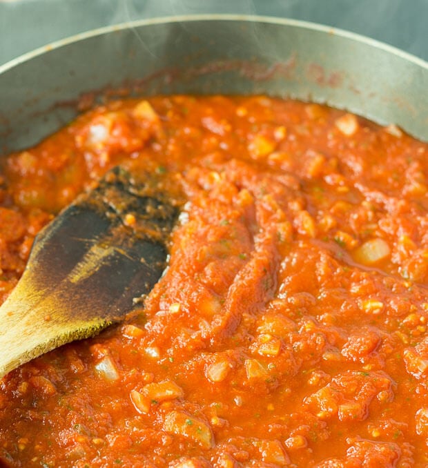 Arrabiata sauce simmering in a pan with a wooden spatula in.