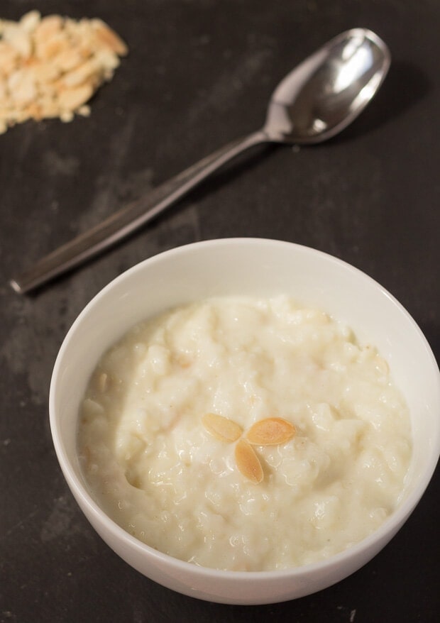 Birds eye view of a bowl of easy rice pudding garnished with flaked almonds and a spoon to eat with at the top.