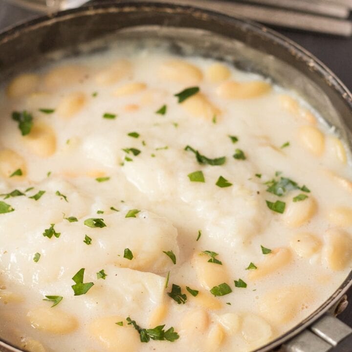 Poached cod with butter beans cooking in a shallow pan.