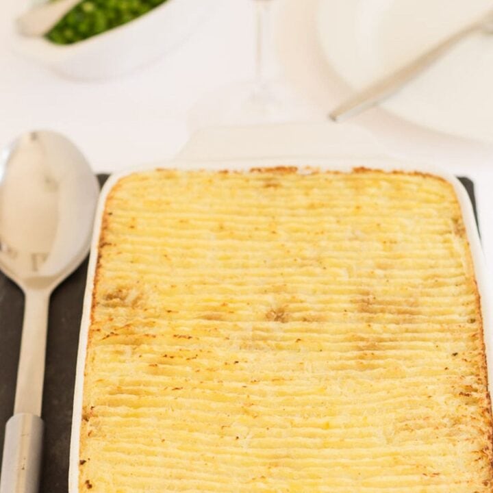 Vegetarian Quorn cottage pie just removed from oven and ready to serve. A glass of red wine and dish of peas at the top.