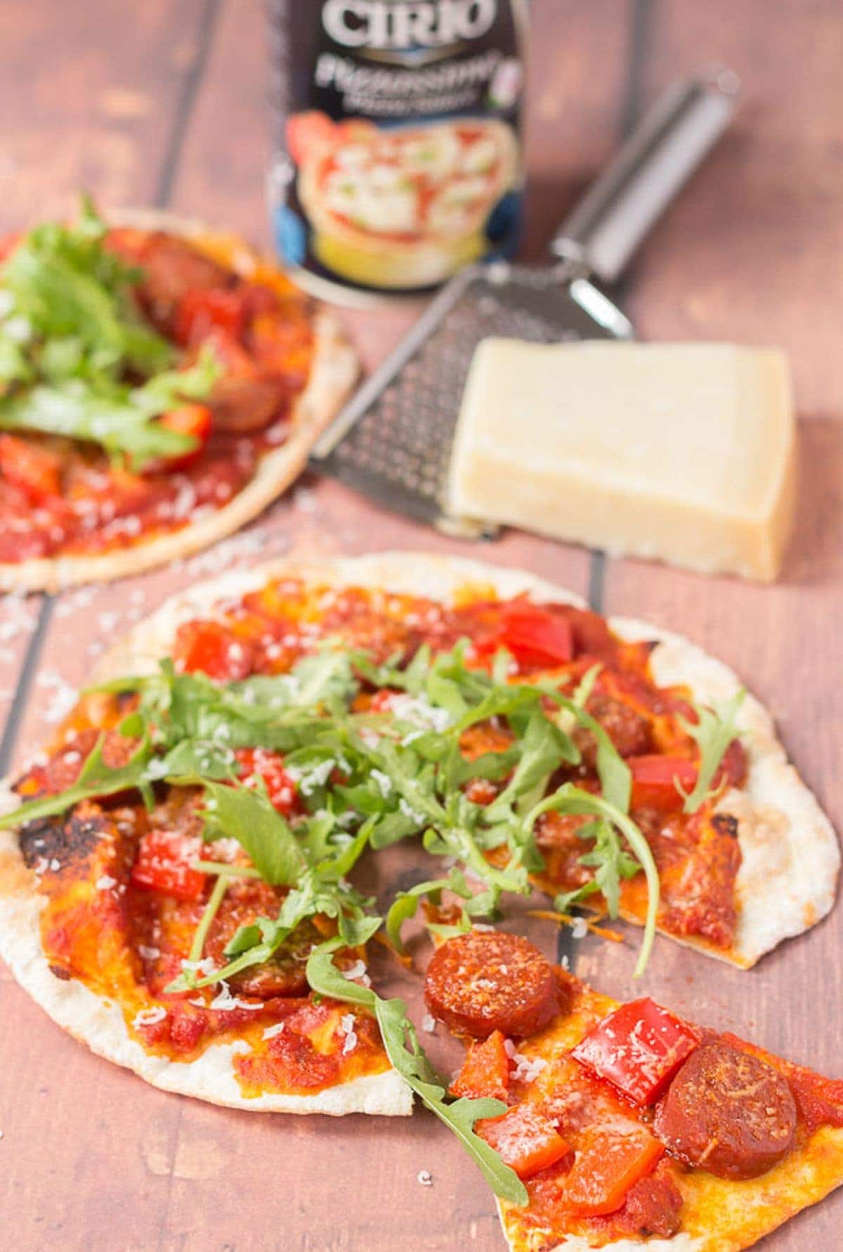 Flatbread pizza with a slice pulled away. Block of cheese, cheese grated and tinned tomatoes in the background.