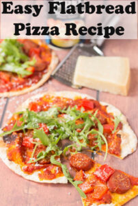 An easy flatbread pizza with a slice taken out of it and a block of parmesan in the background.