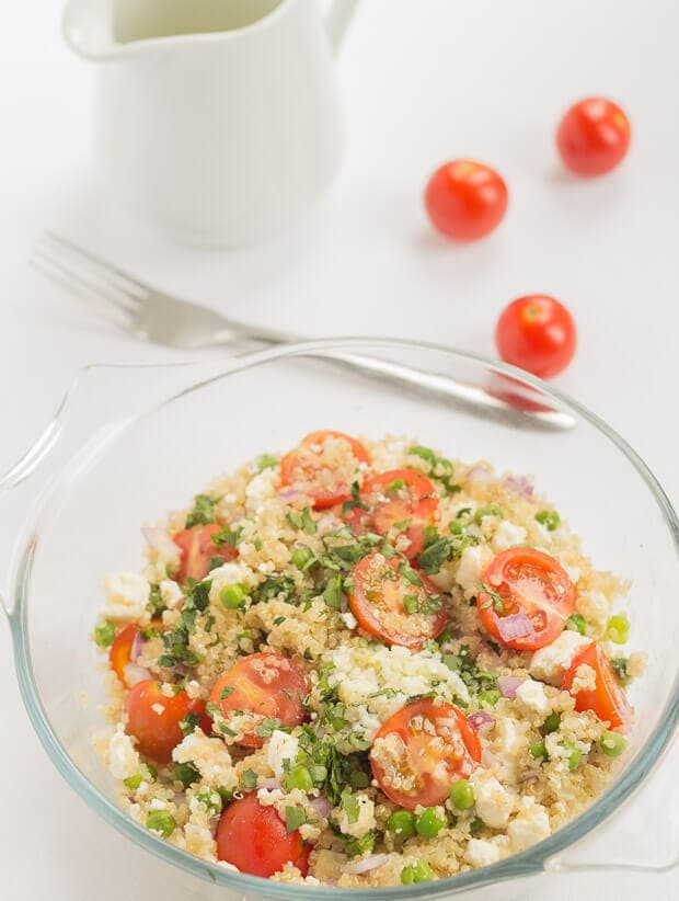 Looking down on a bowl of prepared feta and lemon quinoa salad. A jug, fork and three cherry tomatoes at the top.
