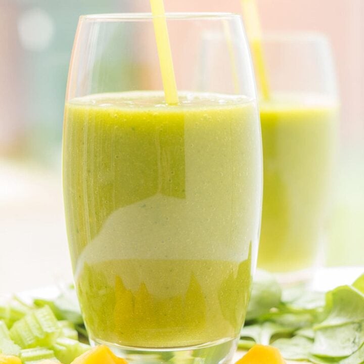Two glasses of orange mango green smoothies with straws in. Sliced oranges at front of glasses.