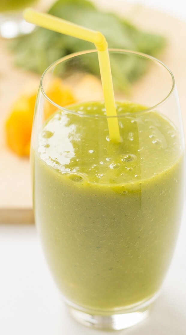 Close up of a glass of orange mango green smoothie with a straw in.