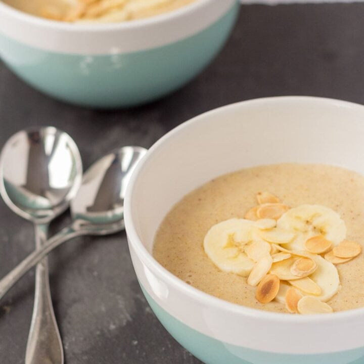 Two bowls of banana millet porridge decorated with sliced bananas diagonally across from each other. Serving spoons to the left.