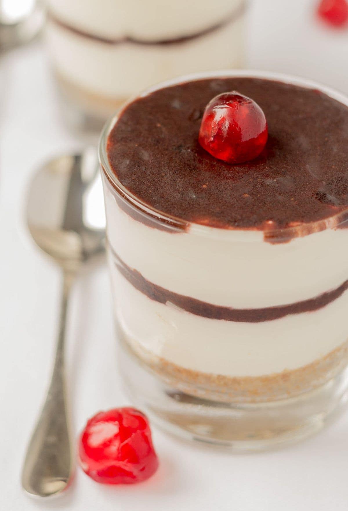 No bake chocolate cherry cheesecake in a glass decorated with a cherry and a dessert spoon to the left hand side.
