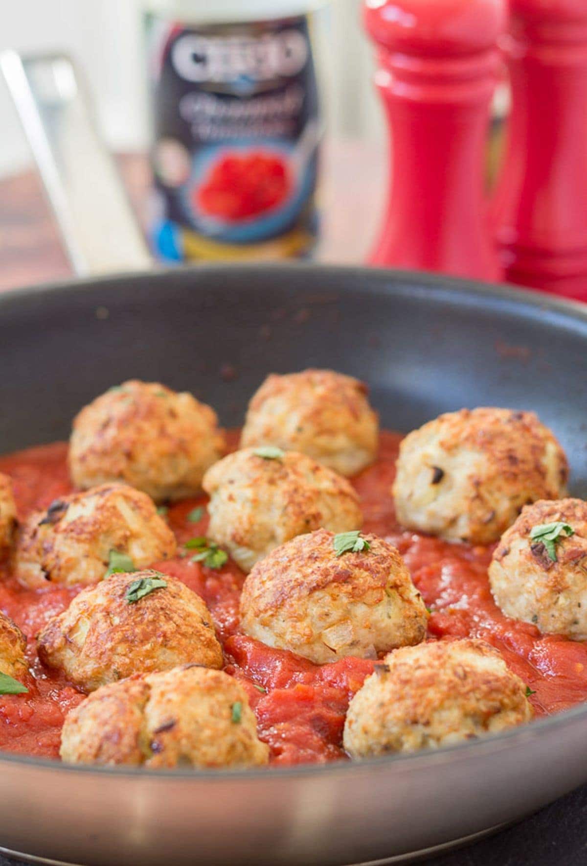 Front view of a pan of baked turkey meatballs in tomato and chilli sauce. Empty tin of tomatoes and salt and pepper cellars in the background.