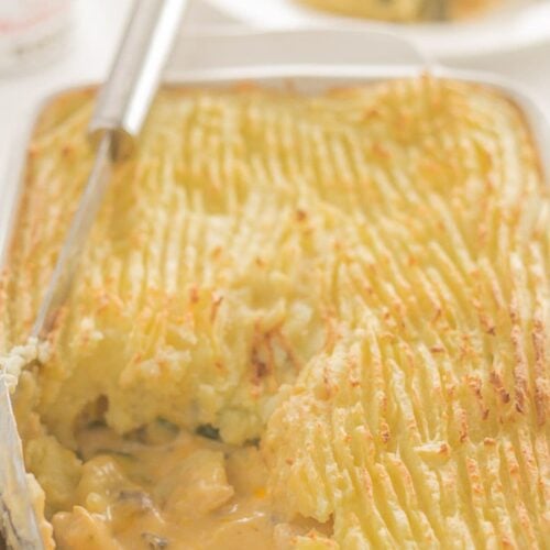 A casserole dish of turkey and courgette bake with a portion taken out and a serving spon on top.