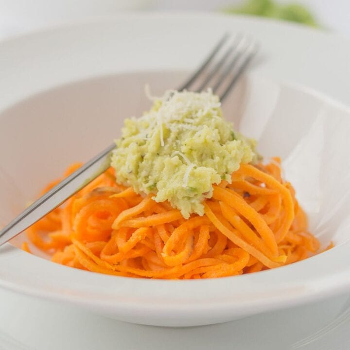 A bowl of spiralized sweet potato topped with brussels sprout pesto and a fork to the side.