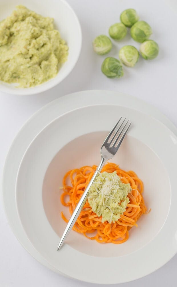 Birds eye view of a bowl of brussels sprout pesto with spiralized sweet potato with a fork to the side. A bowl of the pesto and some sprouts as decoration at the top.