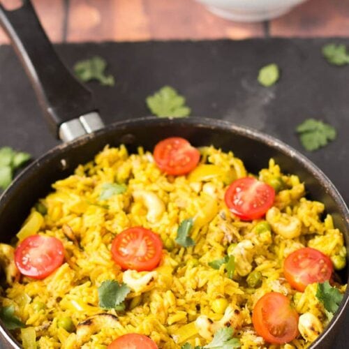Tuna cashew pilau in a pan on a black slate. Two bowls of pilau served in the background.