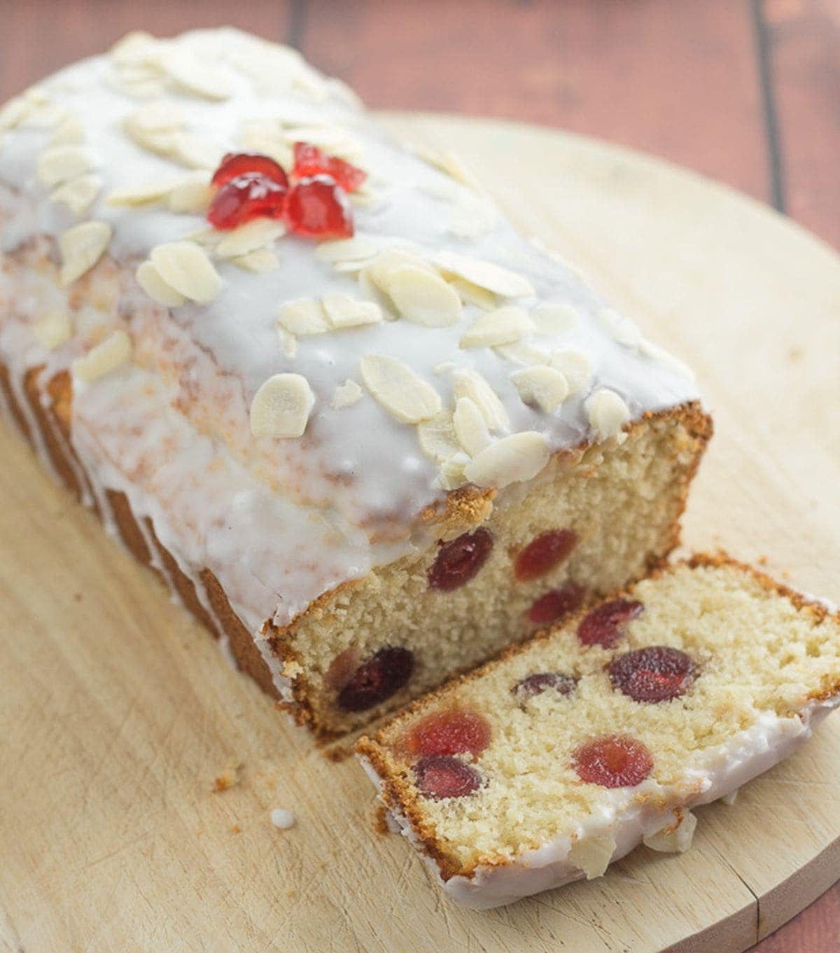 Cherry bakewell loaf cake on a chopping board with a slice taken off the front.
