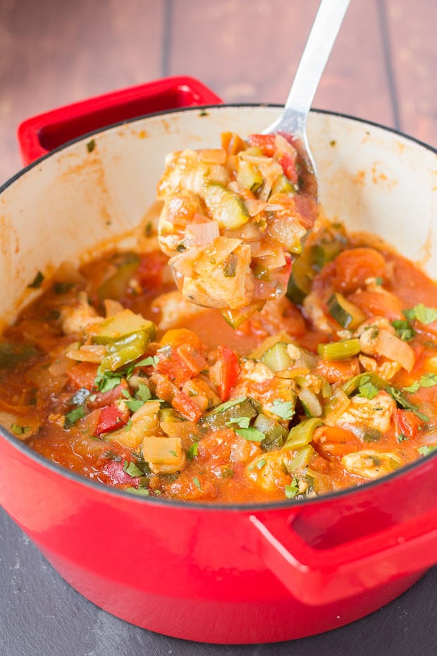 A spoon lifting a portion of Mediterranean chicken from the cooked one pot Mediterranean chicken casserole pot.