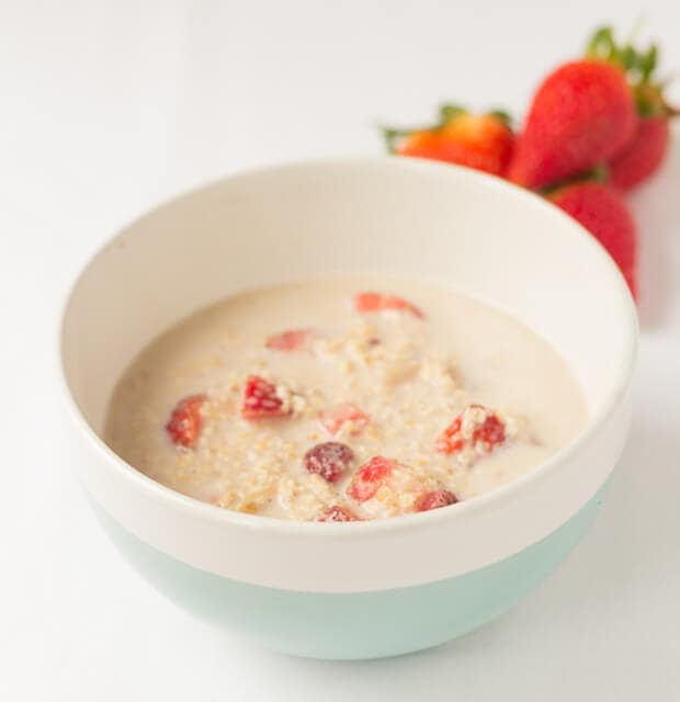 Strawberry vanilla overnight oats in a bowl with four strawberries behind.