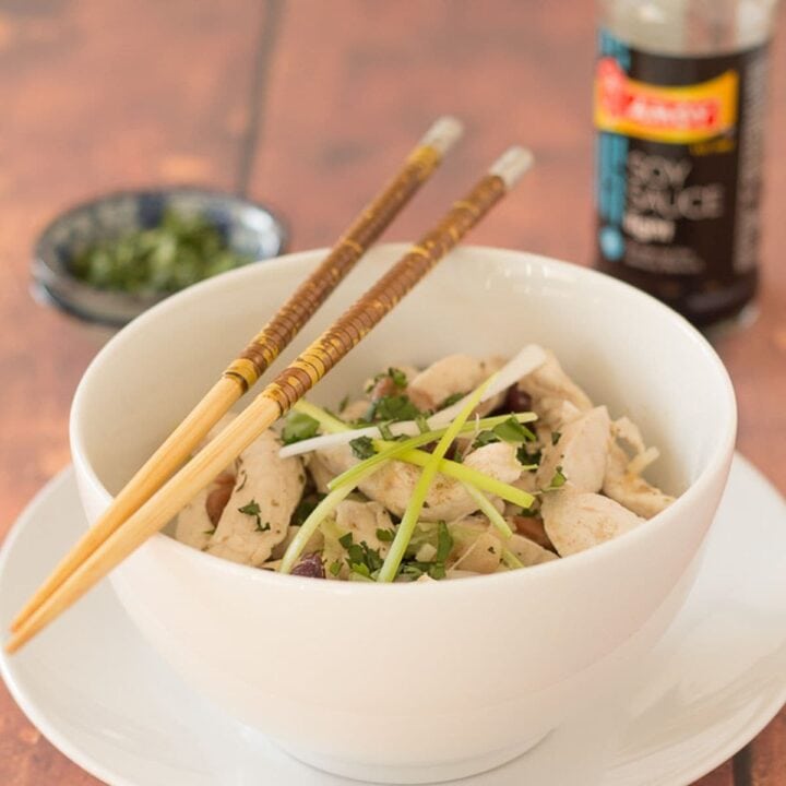 A bowl of chicken and mixed bean stir fry with chopsticks sitting on top. Soy sauce and a dish of chopped coriander in the background.