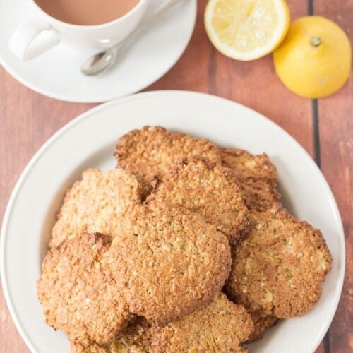 A plate of lemon oat cookies with a cup of tea and a lemon cut in half at the top of the picture.