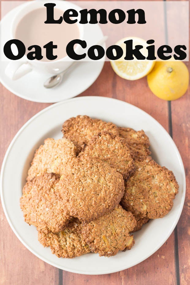 A plate of lemon oat cookies with a cup of tea to the side and a lemon cut in half.