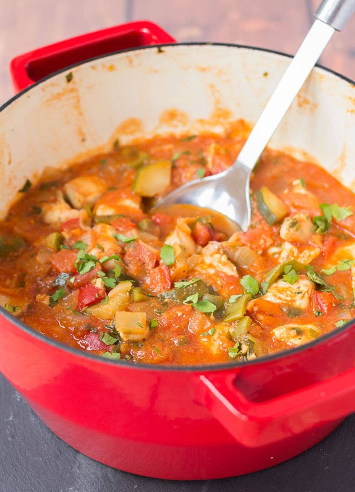 One pot Mediterranean chicken in a large casserole pot with a serving spoon in.