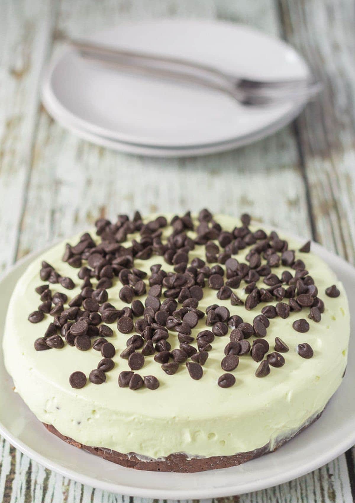 No bake mint chocolate chip cheesecake on a plate. Serving plates and forks in the background.